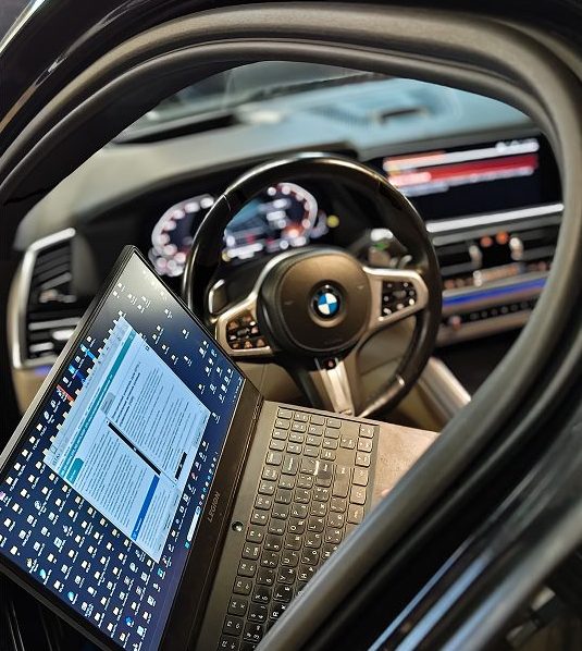 A digital diagnostic laptop being used inside a BMW cabin to perform advanced vehicle programming and system checks.